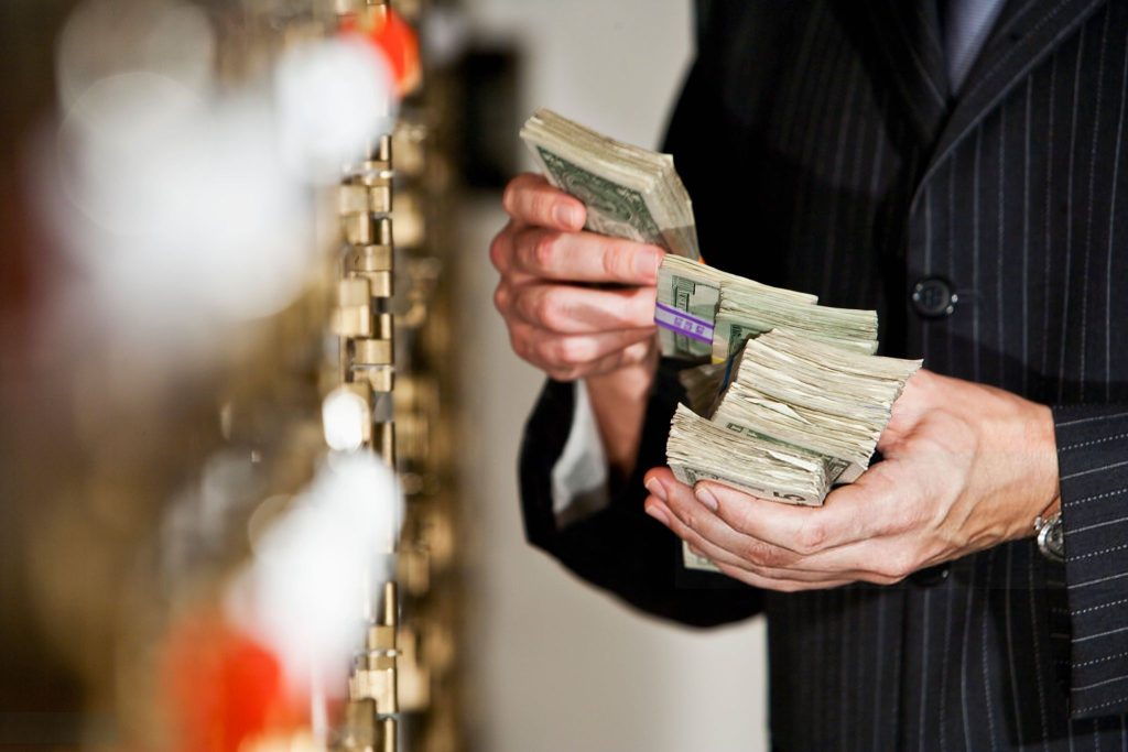 Man holding big stack of US paper currency by safety deposit boxes. Focus on money