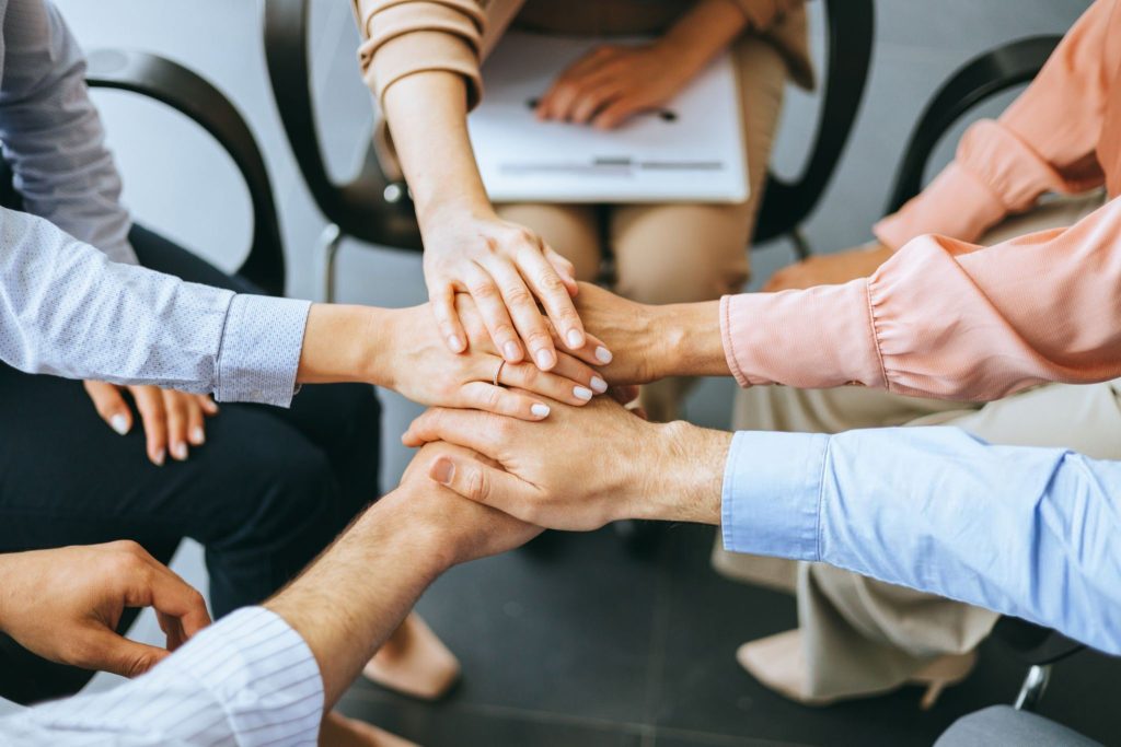 This photo captures a focused view of a team of individuals joining their hands together, depicting a scene of collaboration, trust, and agreement in a professional setup